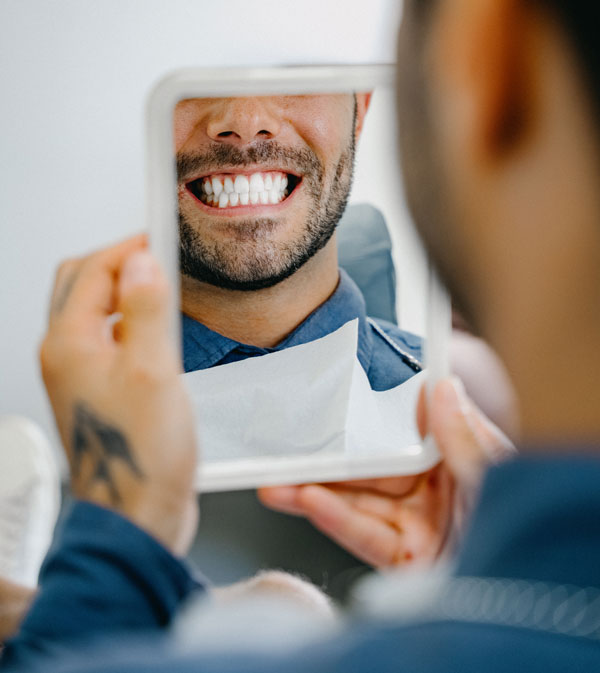 Patient betrachtet sein strahlendes Lächeln nach ästhetischer Zahnbehandlung im Spiegel